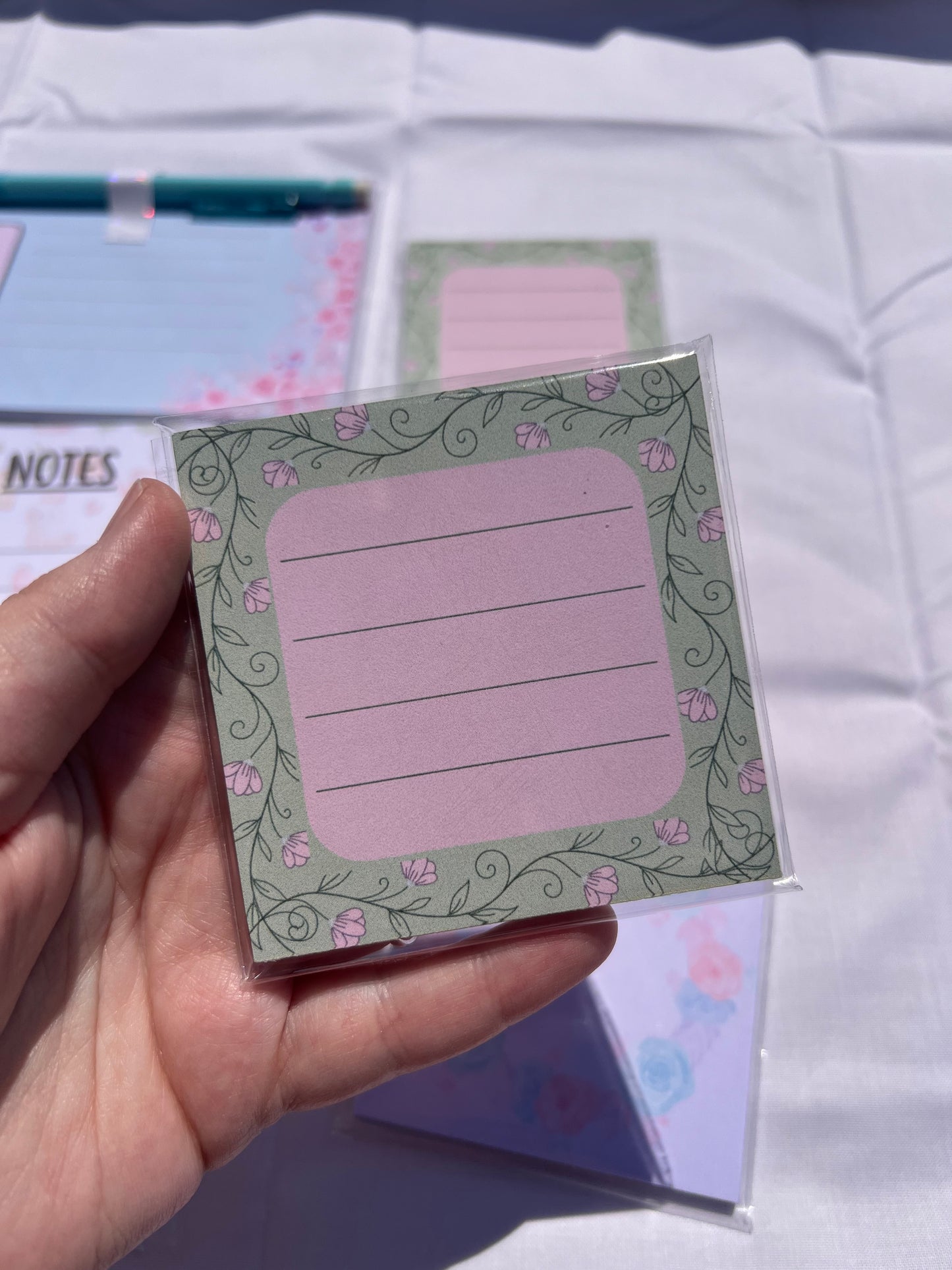 Hand holding a small square notepad with decorative border and text