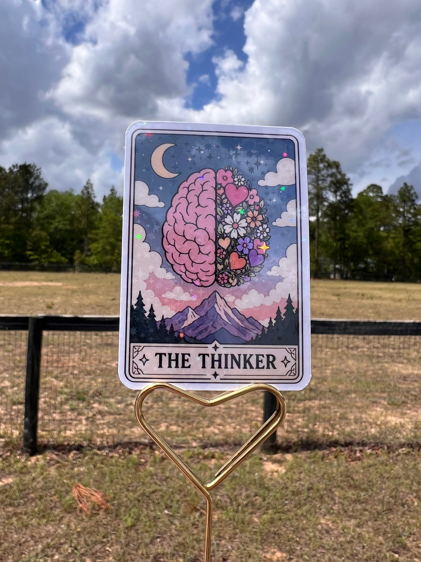 Card with 'The Thinker' design featuring a brain and decorative elements, held by a clip against a natural background.