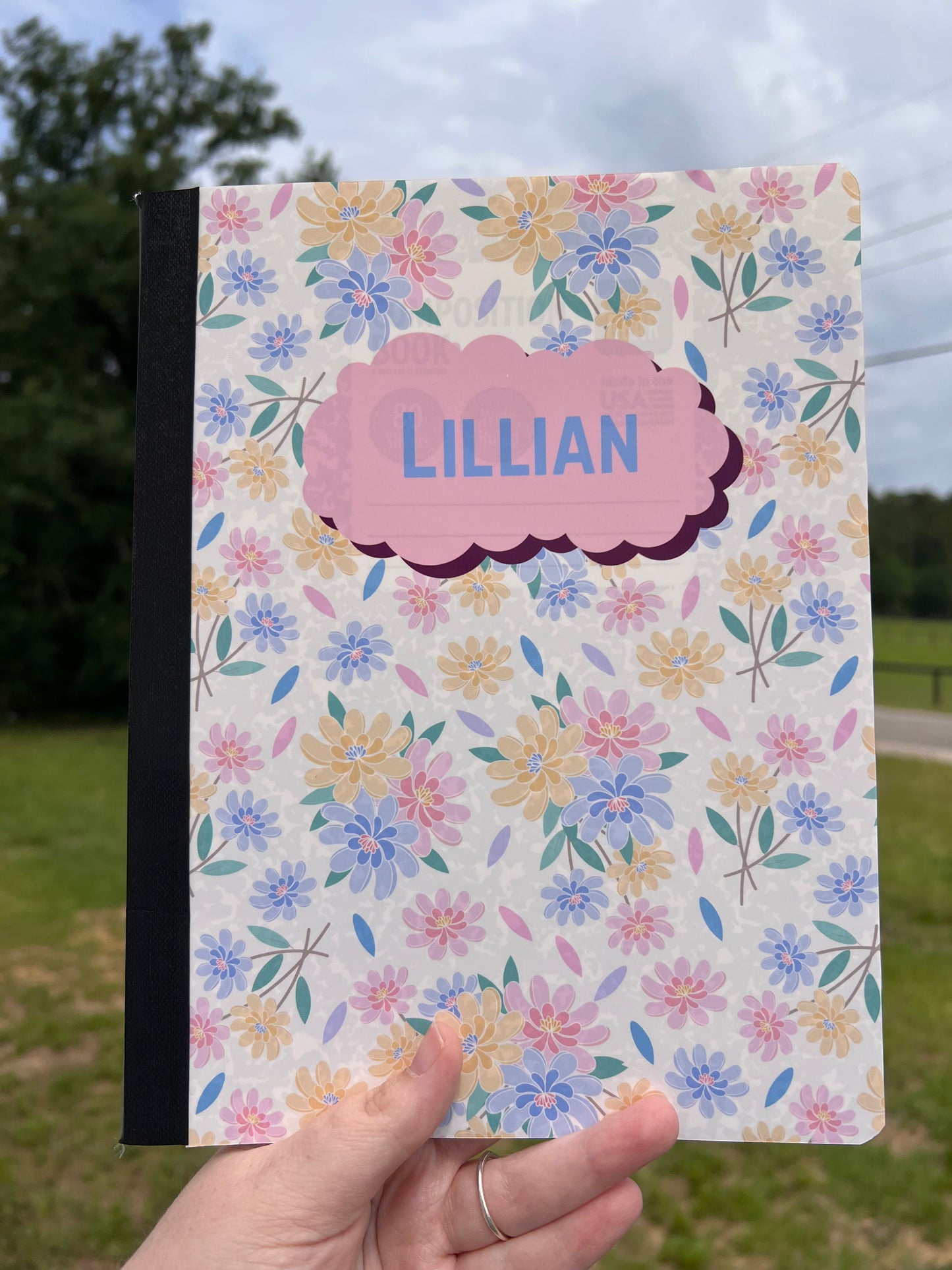 Floral-patterned notebook with 'LILLIAN' on a person's hand against a blurred outdoor background