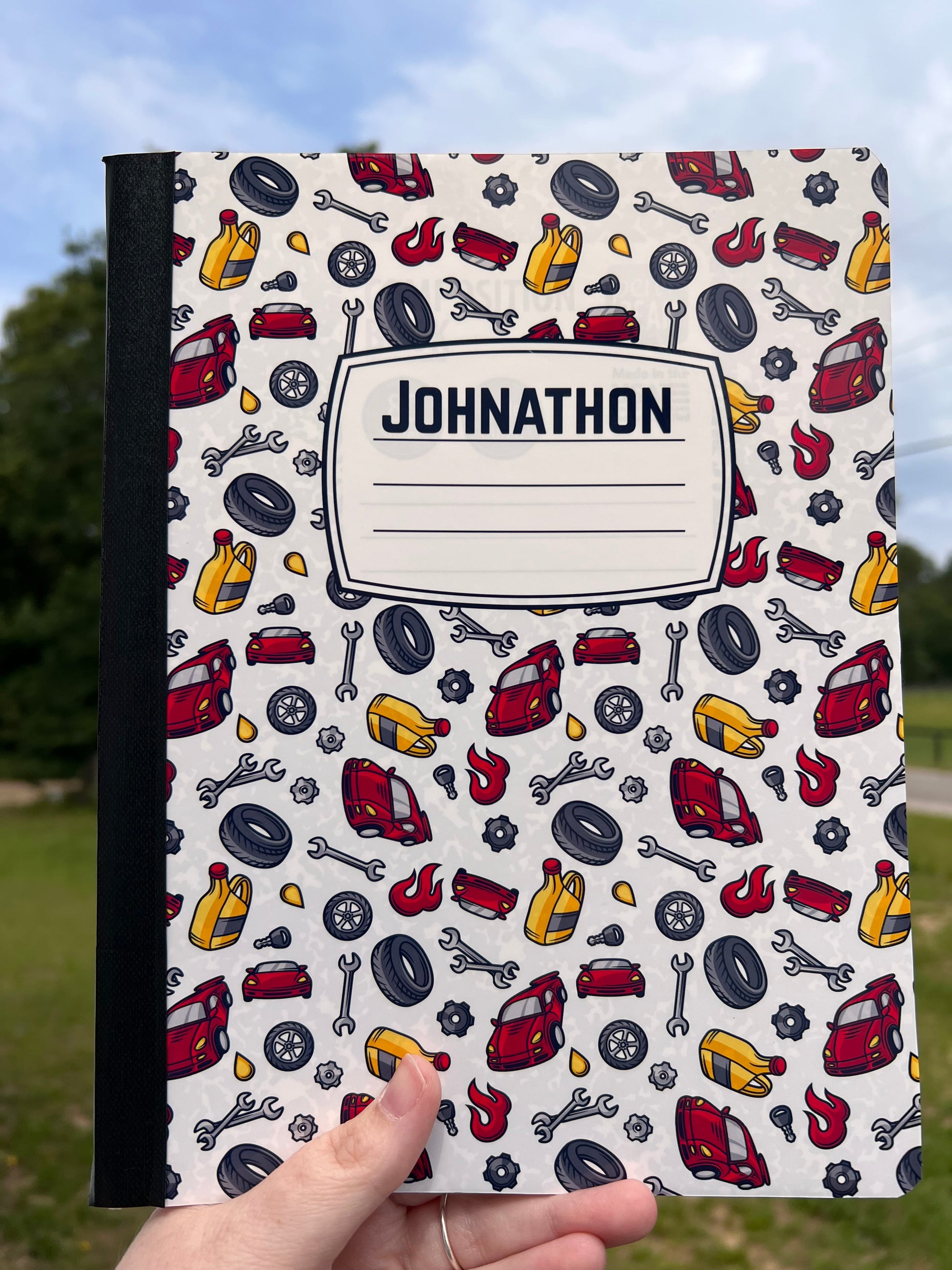 Personalized pouch with car-themed design and name 'Johnathon' held by a hand against a blurred natural background.