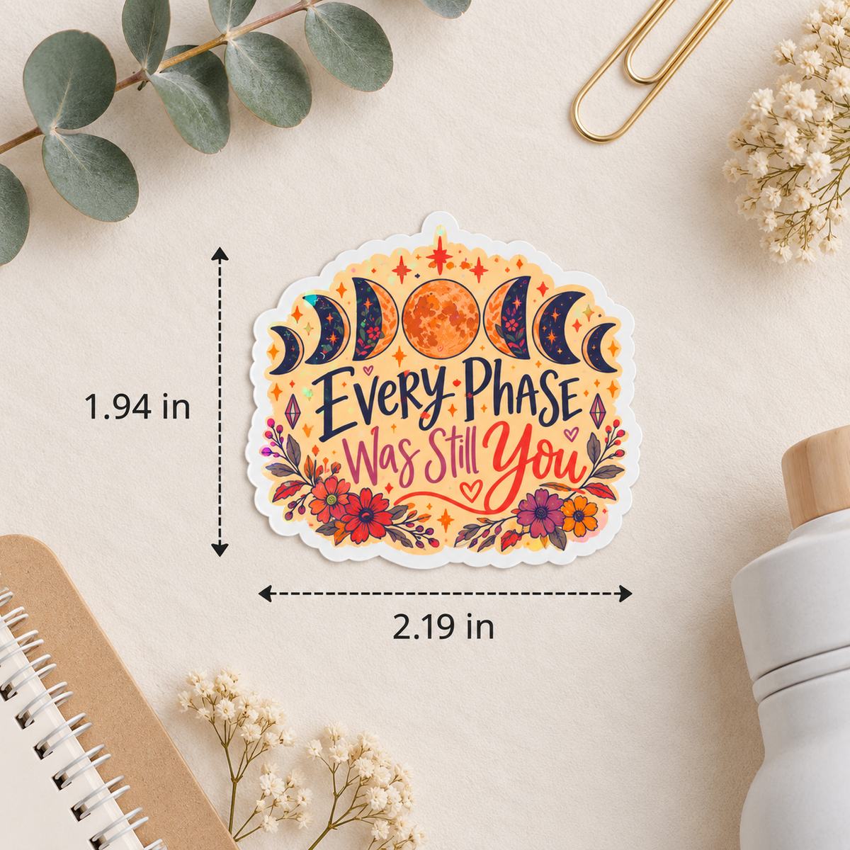 A decorative sticker with a scalloped white border and the phrase “Every Phase Was Still You” in dark lettering, surrounded by moon phases, a sun, and flowers. The sticker is shown on a beige surface with dimension arrows and labels reading 1.