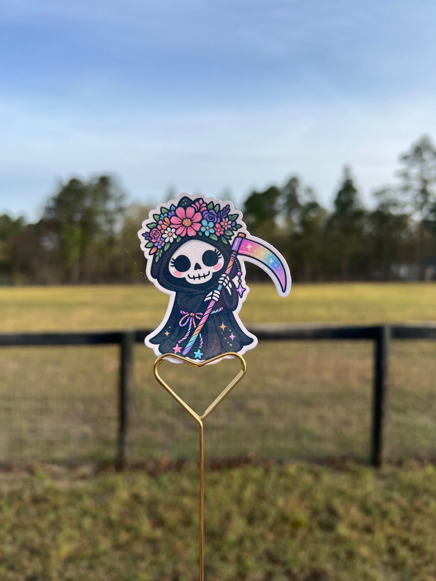 Decorative fish-shaped sticker with floral designs and a rainbow on a metal rod against a blurred outdoor background.