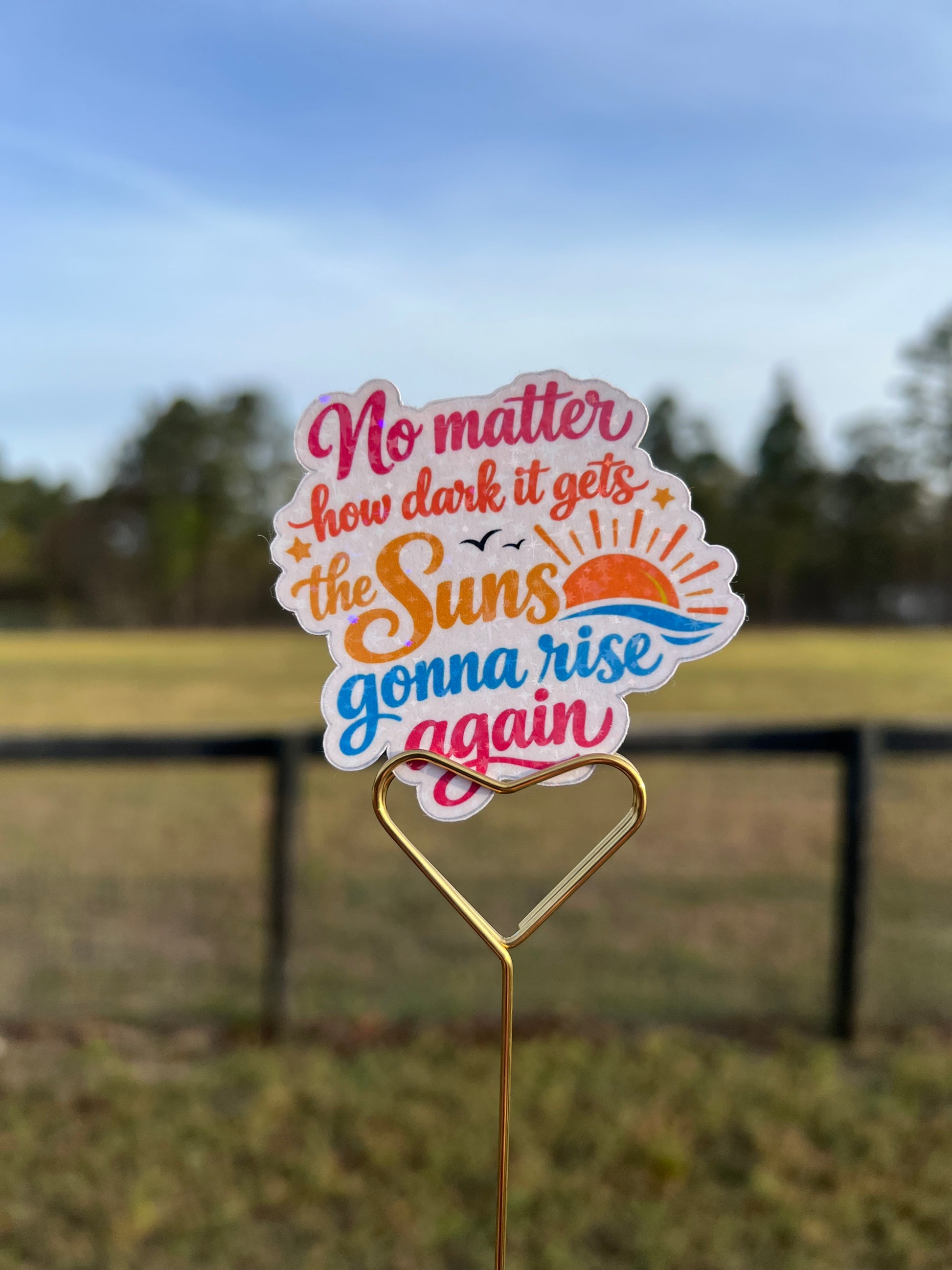 Decorative sticker with motivational quote on a metal stand against a blurred outdoor background