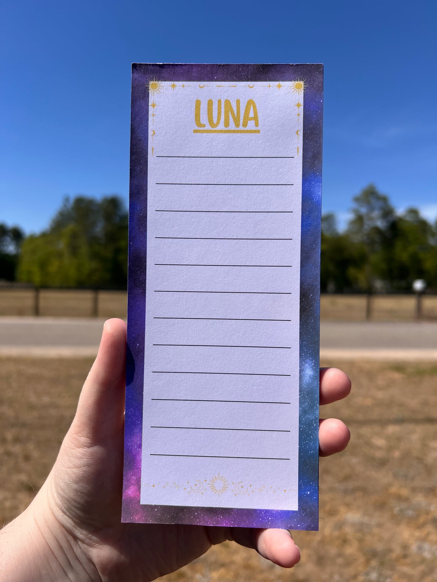 Notepad with 'LUNA' branding held by a hand against a blue sky and building.