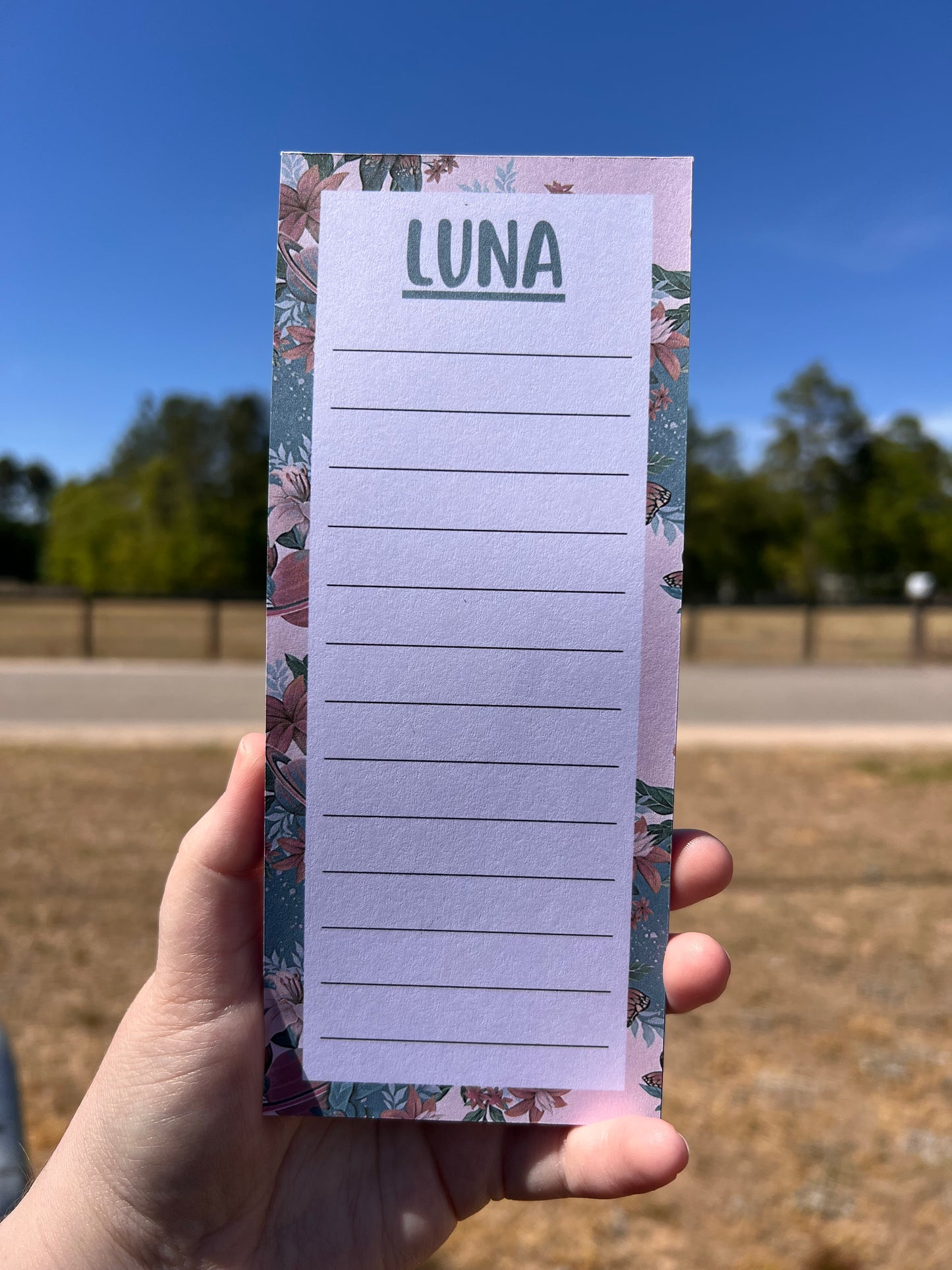 Hand holding a notepad with 'LUNA' branding against a blue sky and building background
