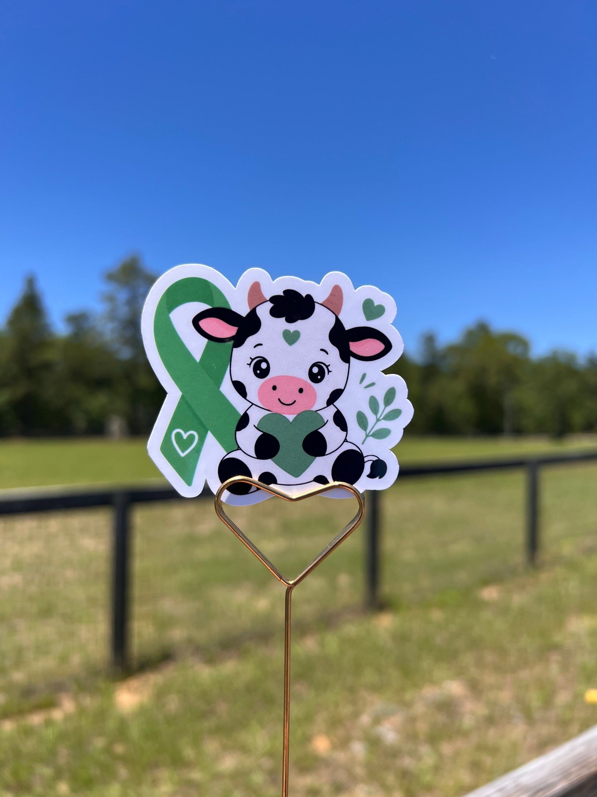 Cartoon cow sticker on a metal clip against a blue sky and grass background