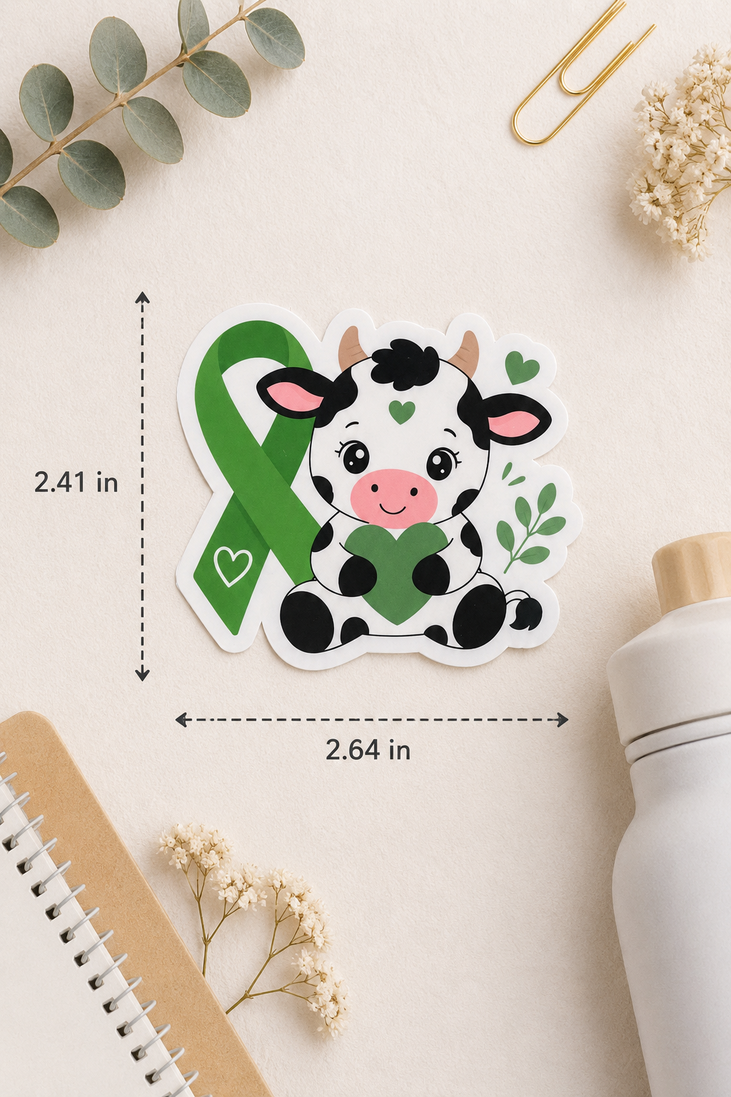 Sticker of a cow with a green ribbon on a light surface with measurements indicated.