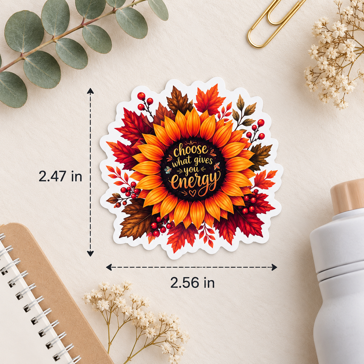 A die-cut sticker featuring a sunflower and autumn leaves with the text 'choose what gives you energy' in the center, shown on a desk flat-lay with measurement arrows and labels indicating 2.47 in height and 2.