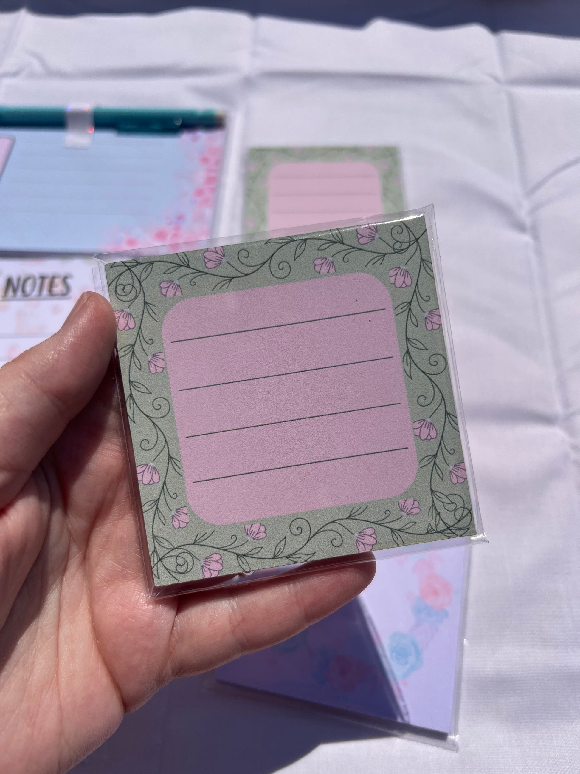 Hand holding a small square notepad with decorative border and text