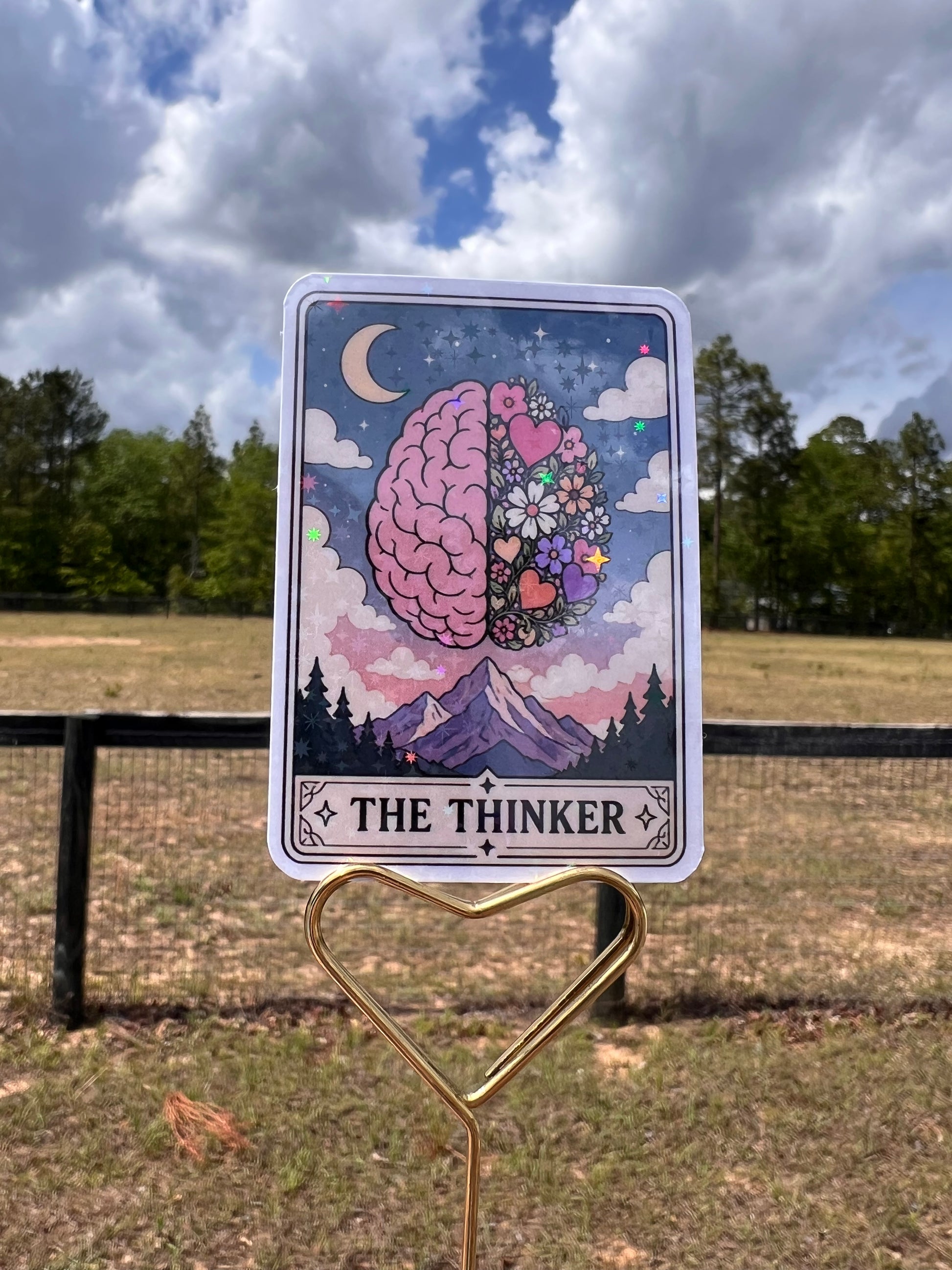 Card with 'The Thinker' design featuring a brain and decorative elements, held by a clip against a natural background.